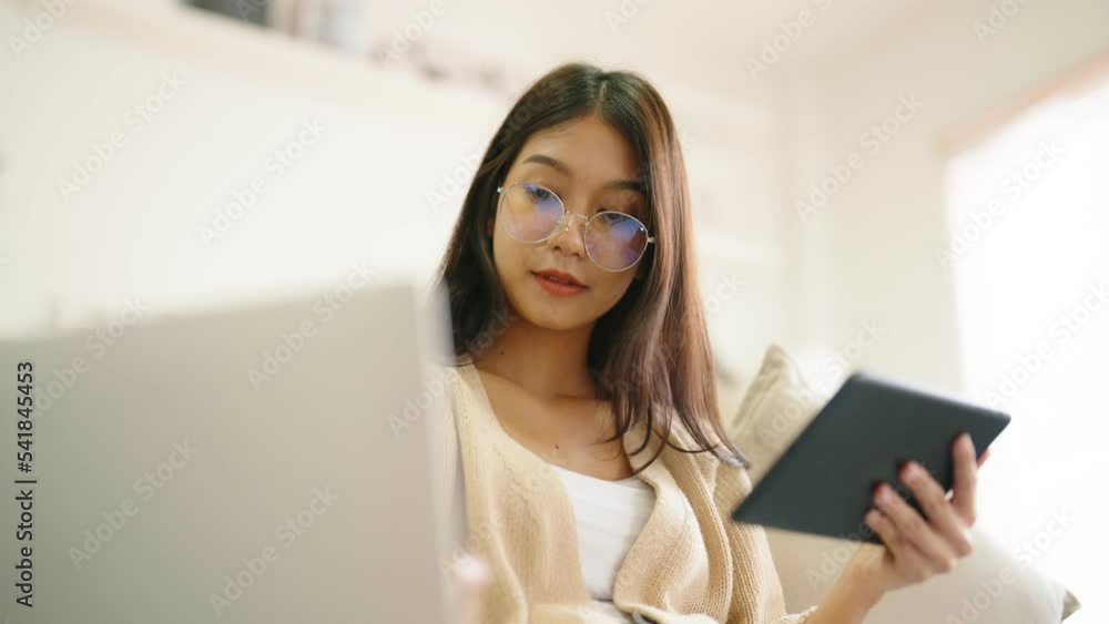 Young asian woman wearing glasses and using tablet while seated on couch at home Young asian woman wearing glasses and using tablet while seated on couch at home