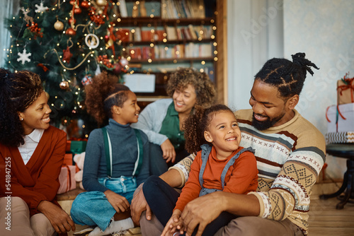 Happy black father and daughter talk while celebrating Christmas with their family at home.