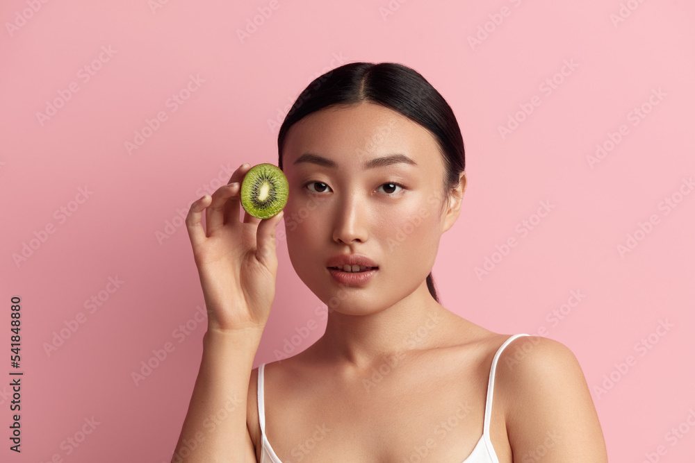 Healthy Nutrition. Portrait Of Asian Woman Posing with Green Kiwi. Portrait of Pretty Girl Looking Camera with Fruit at her Hands. Healthy Food and Dieting Concept Healthy Nutrition. Portrait Of Asian Woman Posing with Green Kiwi. Portrait of Pretty Girl Looking Camera with Fruit at her Hands. Healthy Food and Dieting Concept