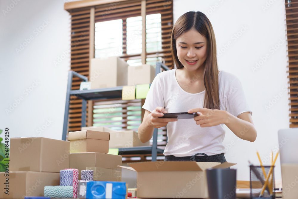 Online business concept, Asian business women take a picture while packing product into parcel box Online business concept, Asian business women take a picture while packing product into parcel box