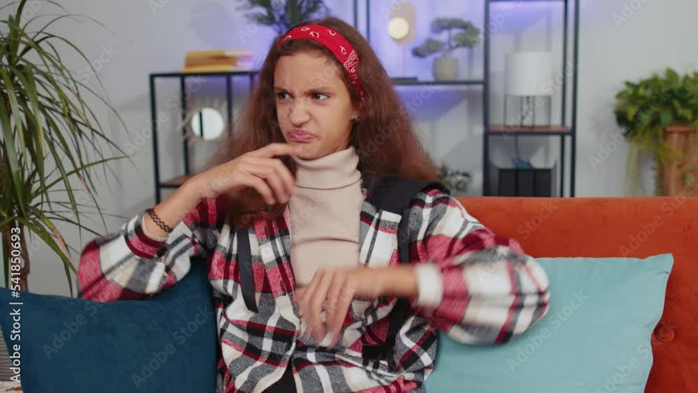 Dislike. Upset girl showing thumbs down sign gesture, expressing discontent, disapproval, dissatisfied bad work at modern home apartment indoors. Displeased young child, kid in living room on sofa Dislike. Upset girl showing thumbs down sign gesture, expressing discontent, disapproval, dissatisfied bad work at modern home apartment indoors. Displeased young child, kid in living room on sofa