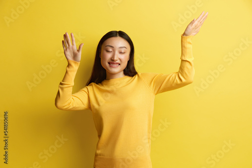 Asian Woman Dancing Isolated. Portrait of Ecstatic Overjoyed Lady Dancing with Raised Arms, Smiling Excitedly, Celebrating Victory, Success. Indoor Studio Shot Isolated on Yellow Background 
