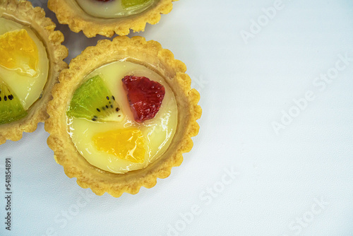 A small plate of a typical Indonesian snack called Pie Susu topped with slices of orange, strawberry and kiwi, served on a white background
