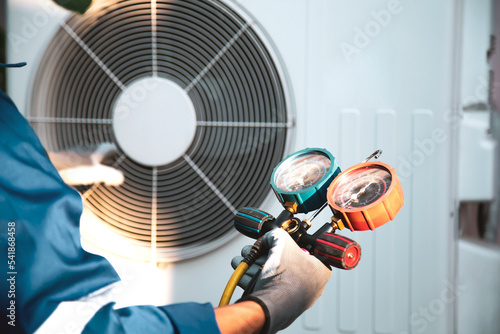 Foto Mechanic air conditioner technician using manifold gauge checking refrigerant for filling home air conditioning and air duct cleaning and maintenance outdoor compressor unit