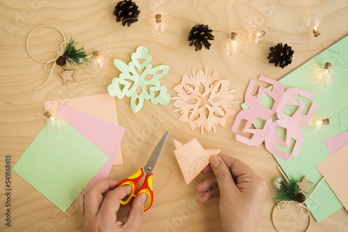 Colorful paper snowflakes cutouts, on a wooden background. Cutting snowflakes from colored paper. Snowflake winter background. Simple winter kids crafts idea.