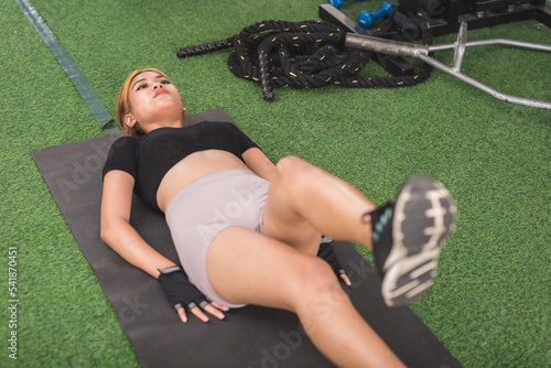 A fit and slim lady does scissor kicks while lying on a black mat at the gym. Working out abs and core. photo