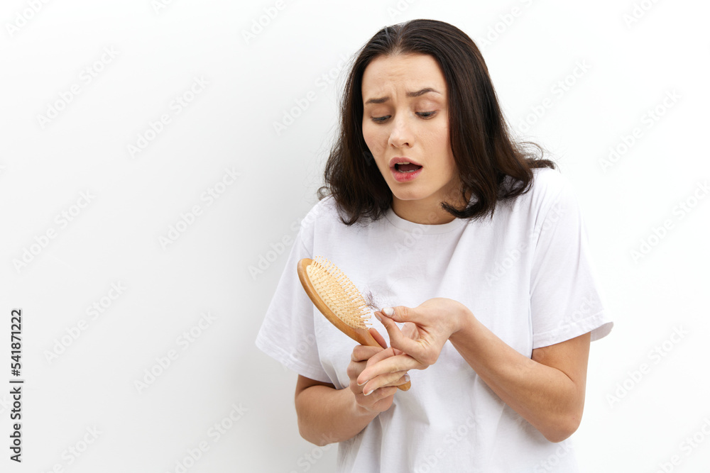 a funny, emotional, sad woman stands in a white T-shirt on a white background and looks sadly at the comb funny raising her eyebrows holding the fallen hair in her hand a funny, emotional, sad woman stands in a white T-shirt on a white background and looks sadly at the comb funny raising her eyebrows holding the fallen hair in her hand
