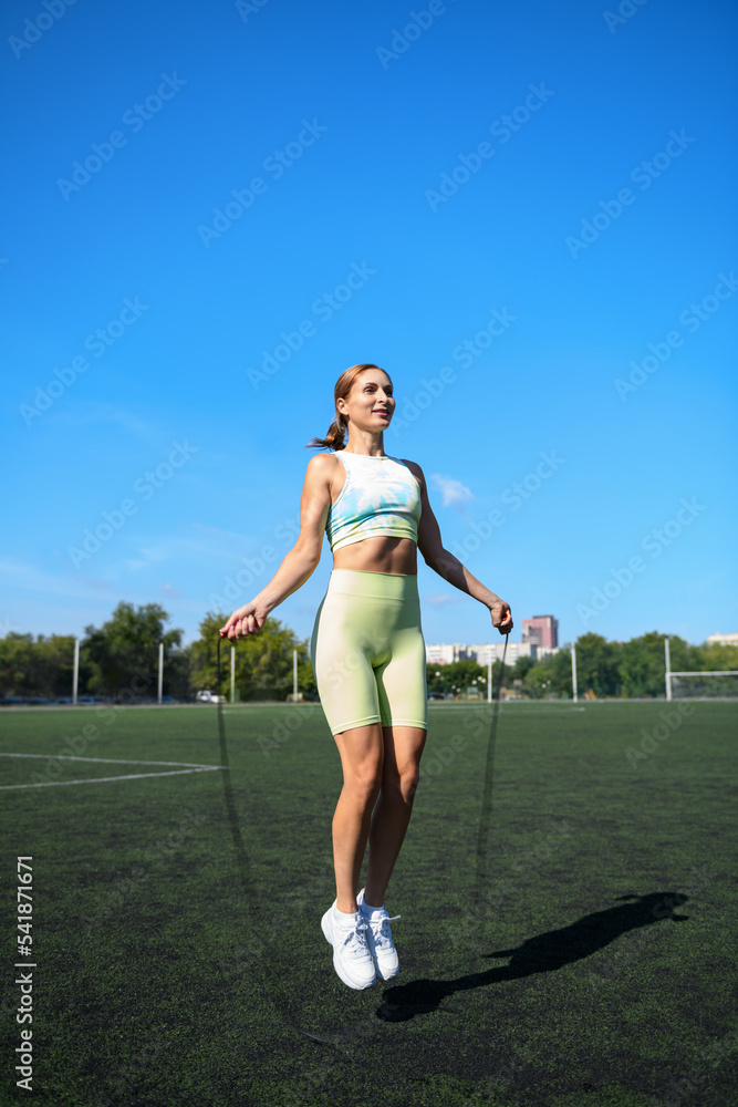 Women and sport. Beautiful girl in summer sportswear jumping rope on the green grass of a football stadium. Middle aged sportswoman Women and sport. Beautiful girl in summer sportswear jumping rope on the green grass of a football stadium. Middle aged sportswoman