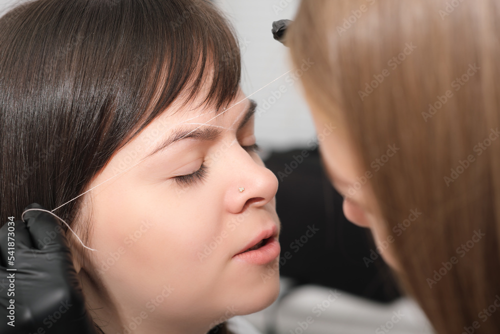 Fototapeta premium woman client with eyes closed in beauty salon during brow correction procedure. making marks on face of woman to do permanent make up.