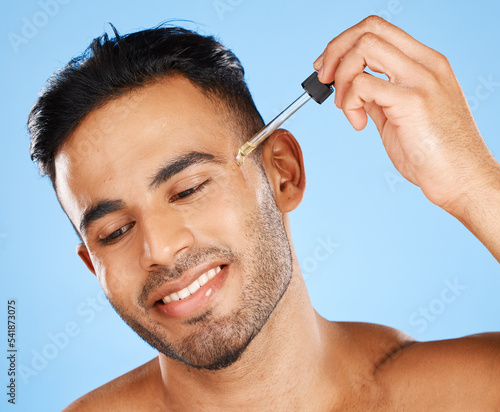 Beard oil, skincare serum and young man face makeup, hair growth product and wellness on blue background. Happy arab guy model drop essential oil, hyaluronic acid and body cosmetics for dermatology