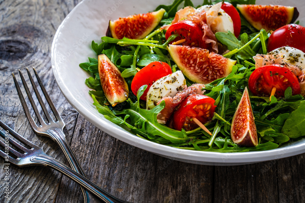 Fresh salad - mozzarella, crudo ham, fig, cherry tomatoes and leafy greens on wooden table
Fresh salad - mozzarella, crudo ham, fig, cherry tomatoes and leafy greens on wooden table