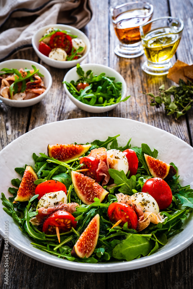 Fresh salad - mozzarella, crudo ham, fig, cherry tomatoes and leafy greens on wooden table
Fresh salad - mozzarella, crudo ham, fig, cherry tomatoes and leafy greens on wooden table