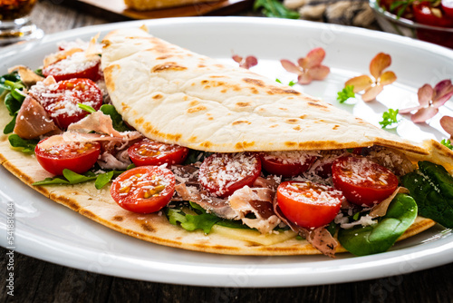 Italian piada wraps - piadina stuffed with fresh vegetable leaves, parmesan and prosciutto crudo on wooden table

