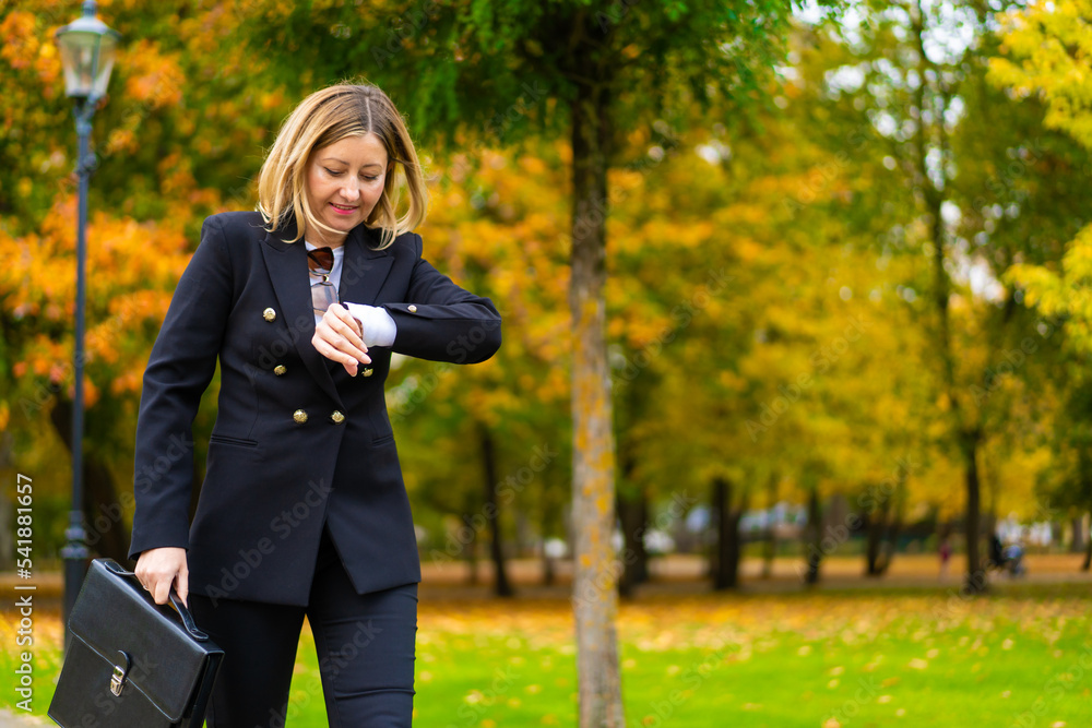 Beautiful woman walking in city park looking at watch going to business meeting
Beautiful woman walking in city park looking at watch going to business meeting