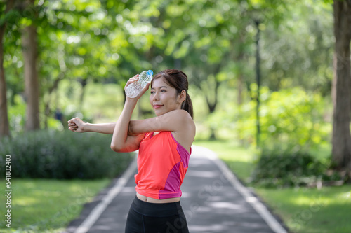 Asian female runner warming up outdoors holding water bottle in the park