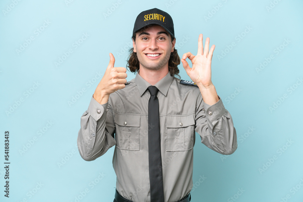 Young safeguard man isolated on blue background showing ok sign and thumb up gesture Young safeguard man isolated on blue background showing ok sign and thumb up gesture