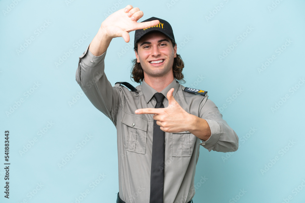Young safeguard man isolated on blue background focusing face. Framing symbol Young safeguard man isolated on blue background focusing face. Framing symbol