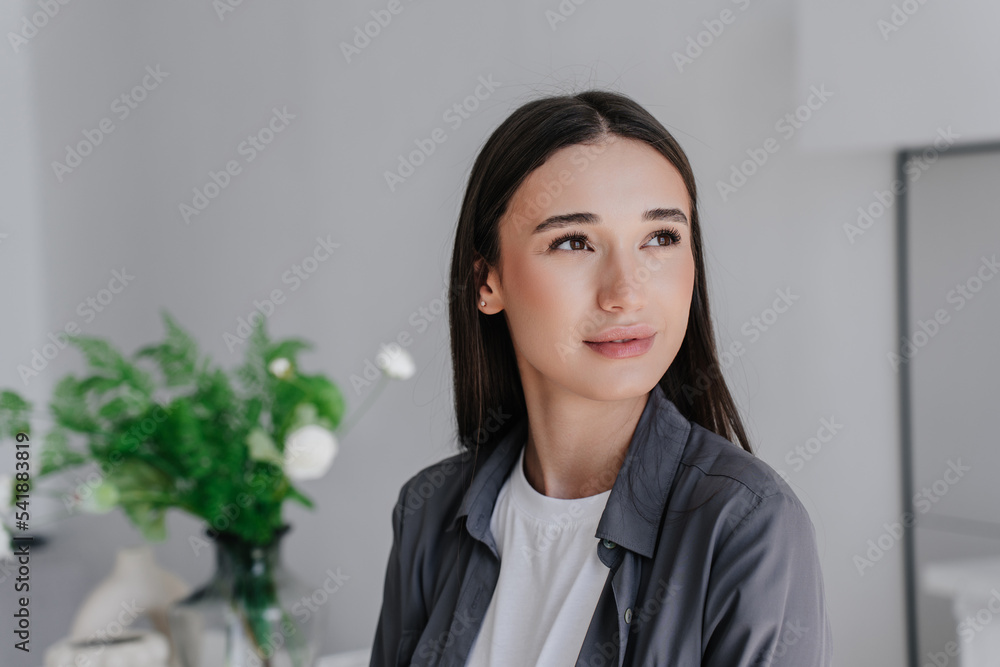 Close up portrait of young purposeful woman in grey shirt looking aside over blurry interior with flowers. Mockup, Youth, dreaming. Attractive young Italian woman with ideal skin. Beauty and health. Close up portrait of young purposeful woman in grey shirt looking aside over blurry interior with flowers. Mockup, Youth, dreaming. Attractive young Italian woman with ideal skin. Beauty and health.