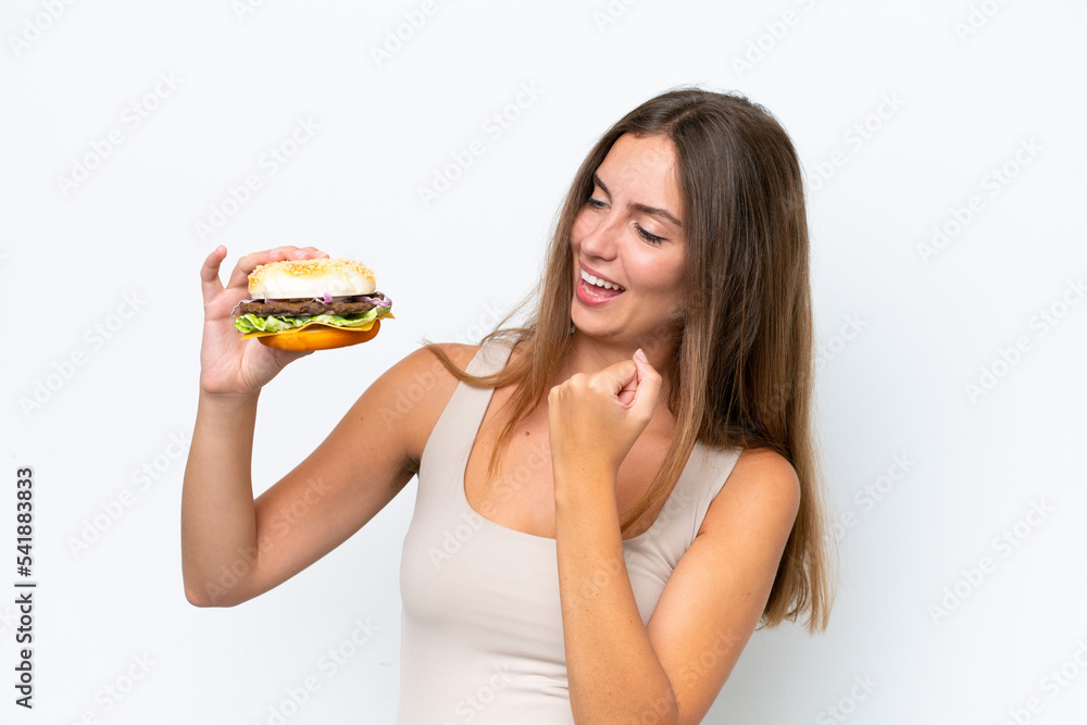 Young pretty woman holding a burger isolated on white background celebrating a victory Young pretty woman holding a burger isolated on white background celebrating a victory