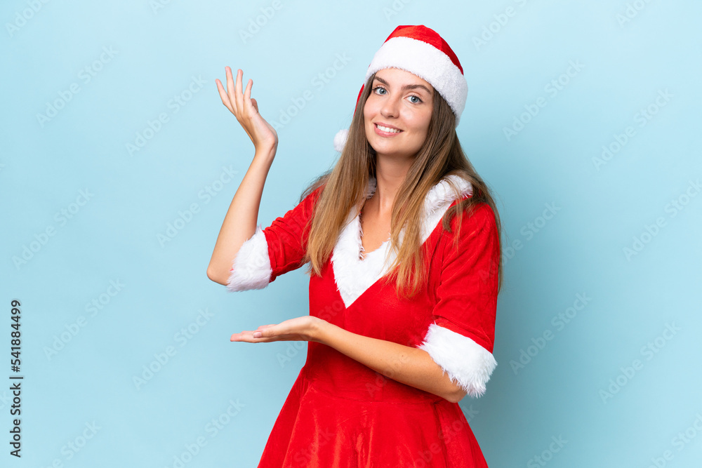 Young caucasian woman dressed as mama noel isolated on blue background extending hands to the side for inviting to come Young caucasian woman dressed as mama noel isolated on blue background extending hands to the side for inviting to come