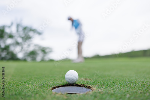 woman golf player putting successfully ball on green, selective focus blur background and clear sky