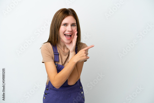 Young English woman isolated on white background pointing to the side to present a product and whispering something