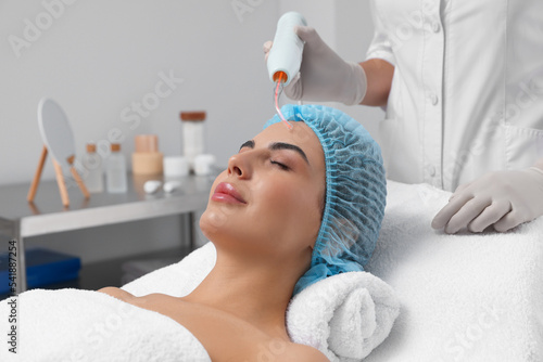 Young woman undergoing face rejuvenation procedure with darsonval in salon photo