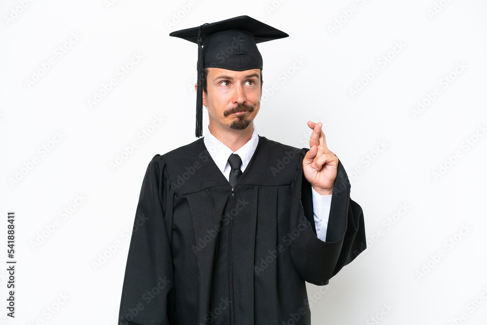 Young university graduate man isolated on white background with fingers crossing and wishing the best Young university graduate man isolated on white background with fingers crossing and wishing the best