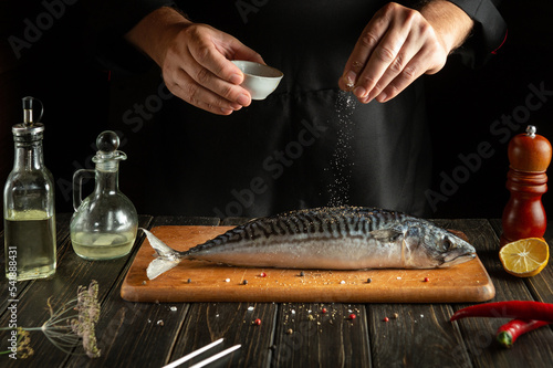 The cook prepares fresh mackerel in the kitchen. Scomber must be salted before baking. European cuisine