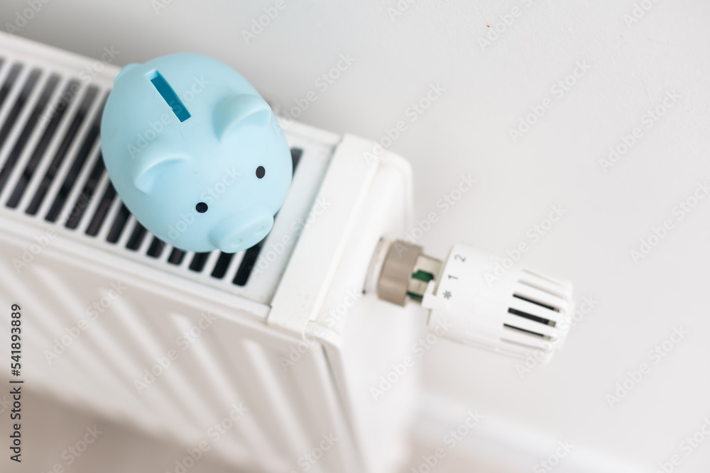 Piggy bank on heating radiator against light background. Space for text. Piggy bank on heating radiator against light background. Space for text.