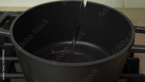 Woman adding water in a pot to boil it at domestic kitchen