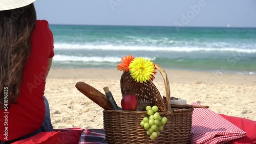 Young girl enjoying picnic on the beach. Summertime relaxation and recreation concept. Blanket with fruits on sandy beach
