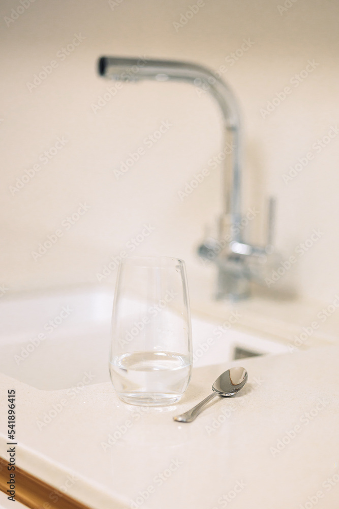 Glass of water and teaspoon on table in kitchen with faucet, closeup. High quality photo Glass of water and teaspoon on table in kitchen with faucet, closeup. High quality photo