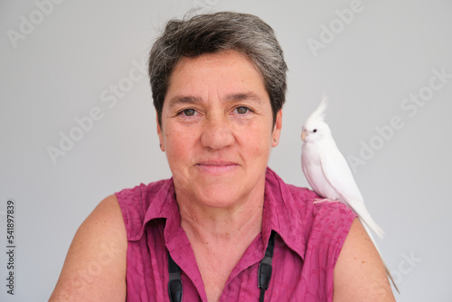 Mature adult woman with her albino cockatiel on her shoulder. White-faced Lutinos mutation.