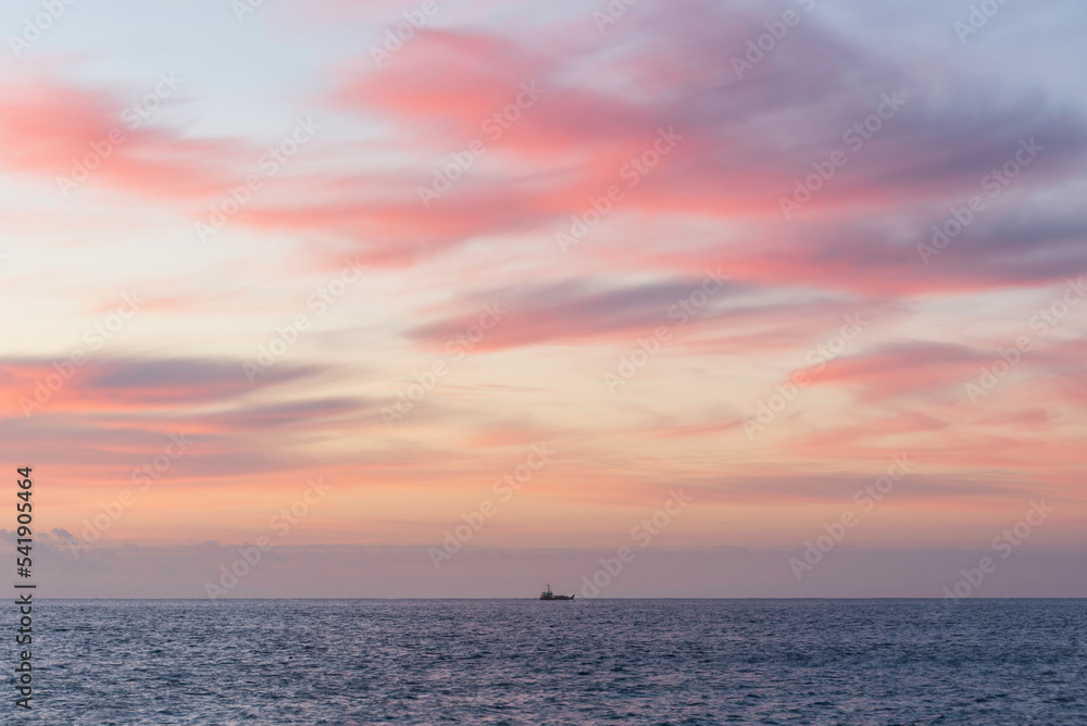 Single fishing trawler boat goes out at dawn with beautiful colors and clouds formations in Cornwall England