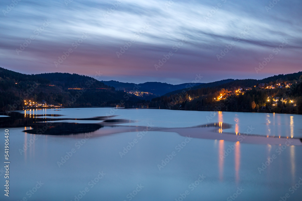 Blue hour after sunset at Titisee in Germany, Black Forest. The still water surface reflects the blue-purple sky 