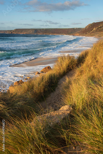 Fototapeta Naklejka Na Ścianę i Meble -  Stunning landscape image of Sennen Cove in Cornwall during sunset viewed from grassy sand dunes with dramatic sky and long exposure sea motion