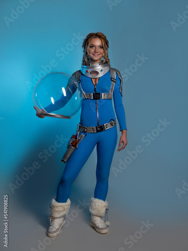 Fantastic astronaut costume in retrofuturism style. A young beautiful blonde in a blue suit with a spherical helmet in her hands. pioneer of space exploration, atomic era, retro style