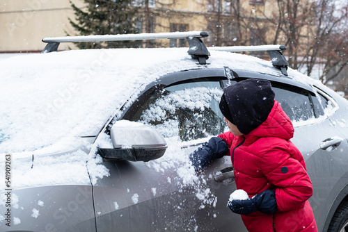 Boy plays with first snow lying on car.