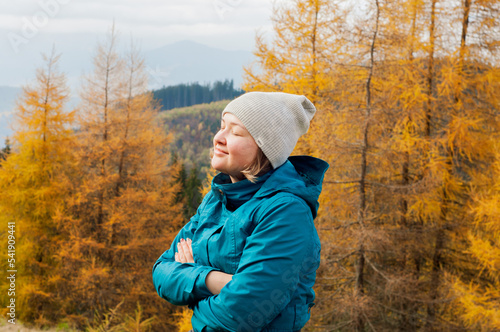 young pretty girl smiling enjoys rest in a hat and jacket against the background of yellow autumn pine trees forest modrina needles in the Carpathians mountains