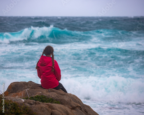 a girl in pigtails watches huge waves during a storm over the ocean in western australia