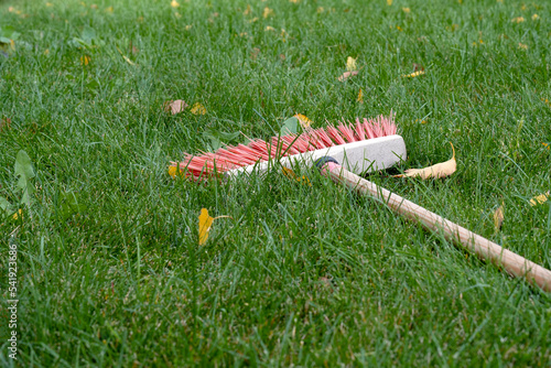 yellow leaves lie on the green grass on the street a wooden broom with red bristles lies on the lawn