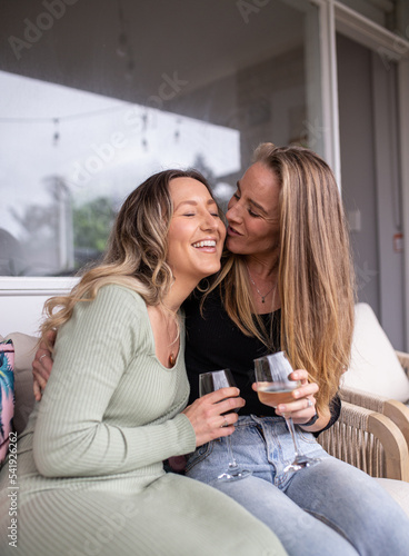 Same sex couple sitting on outdoor chair drinking wine and being affectionate photo