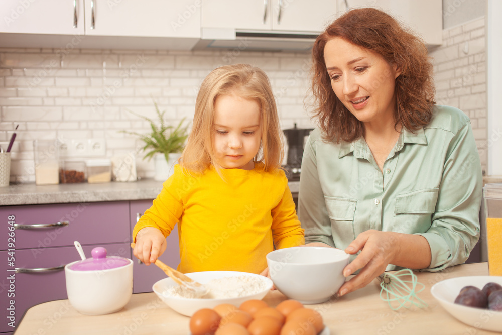 grandmother and granddaughter are making cake in kitchen, happy family, woman and child are smiling. grandmother and granddaughter are making cake in kitchen, happy family, woman and child are smiling.