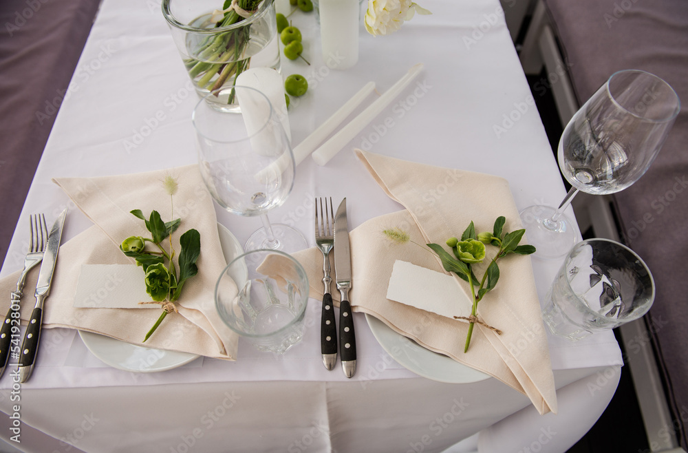Serving the table for the holiday. Festive floral decor on the plates. Place for the inscription of the guest’s name. Beautiful decor for the festive event