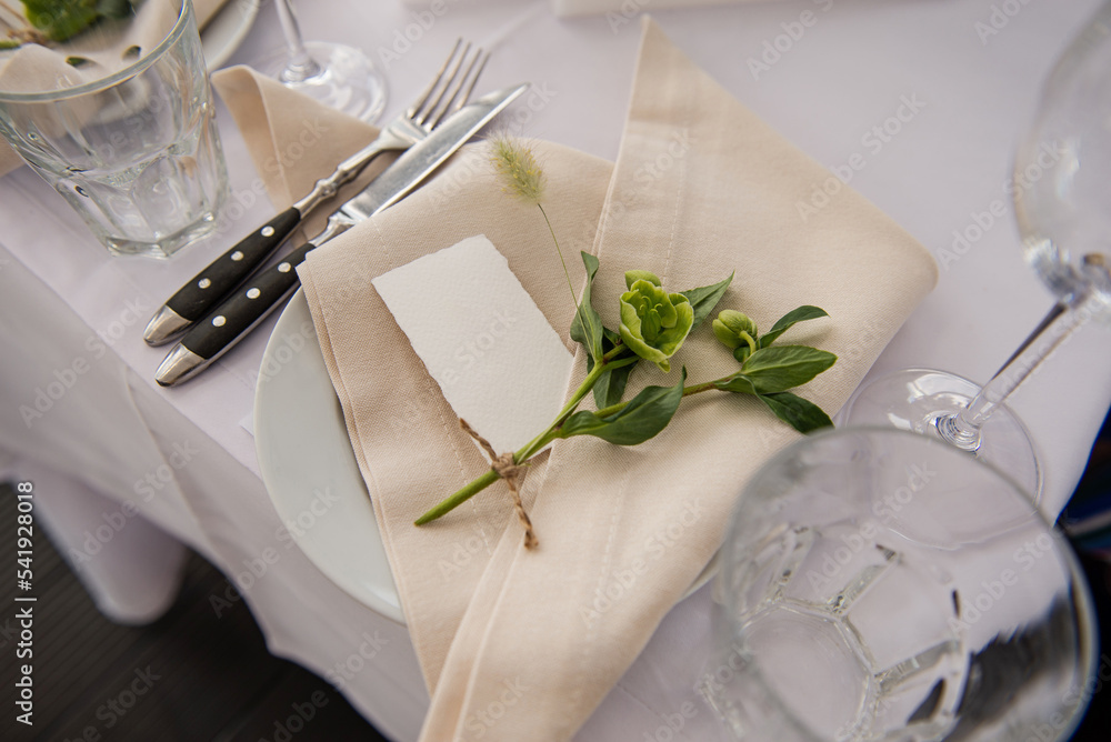 Serving the table for the holiday. Festive floral decor on the plates. Place for the inscription of the guest’s name. Beautiful decor for the festive event