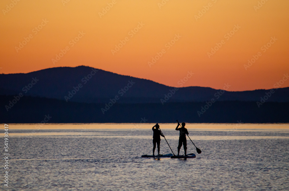 A man and a woman are sailing on a sapa along a mountain lake against the backdrop of sunset. Active family recreation for a healthy lifestyle