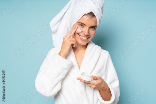 Woman applying facial cream on cheek dressed in bathrobe with head wrapped in towel photo