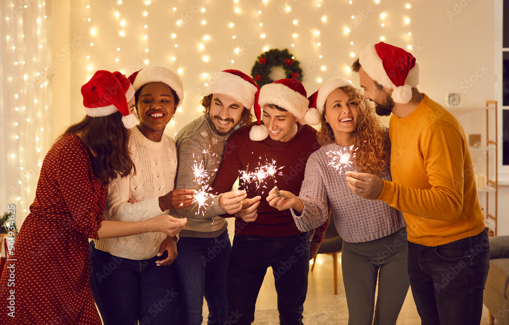 Overjoyed multiracial friends light fireworks celebrate New Year at home together. Smiling diverse international young people have fun enjoy winter holidays Christmas celebration.