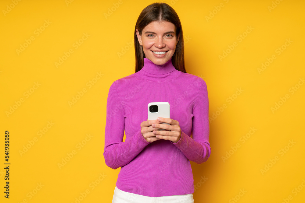 Smiling young woman holding phone, isolated on yellow background Smiling young woman holding phone, isolated on yellow background
